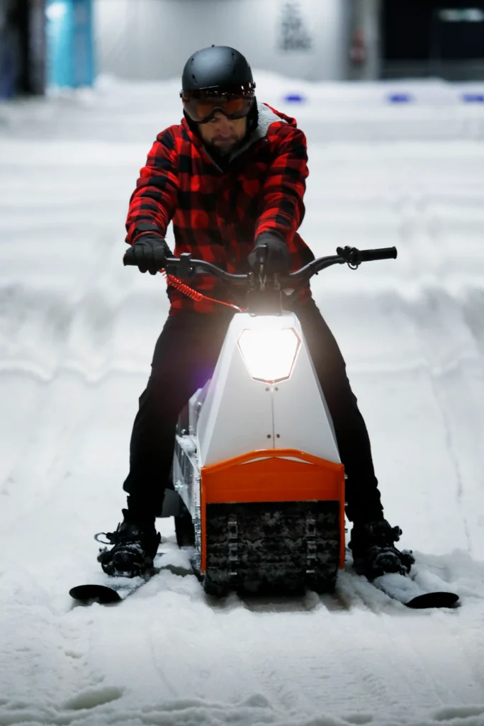 bild på en man som sitter på en el-skoter. Mannen har skidor på fötterna.